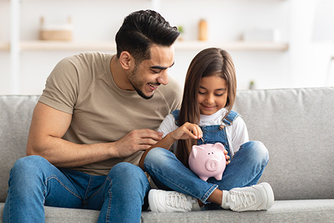dad with his daughter who is holding a piggy bank