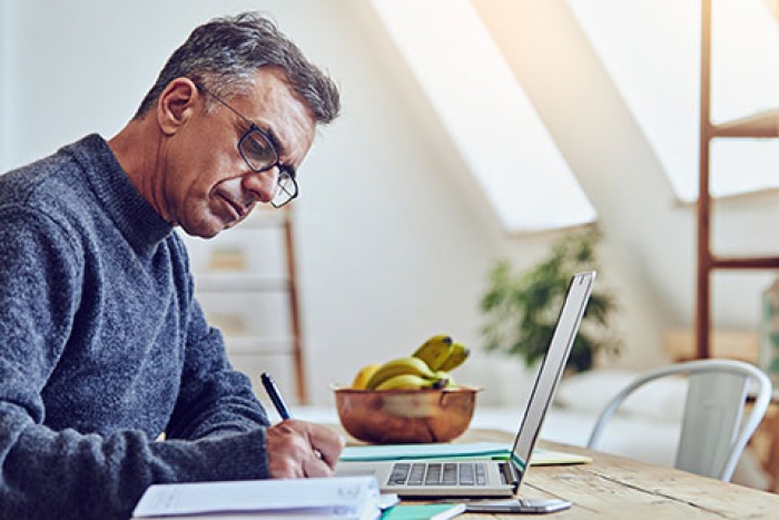 man at table writing in front of laptop