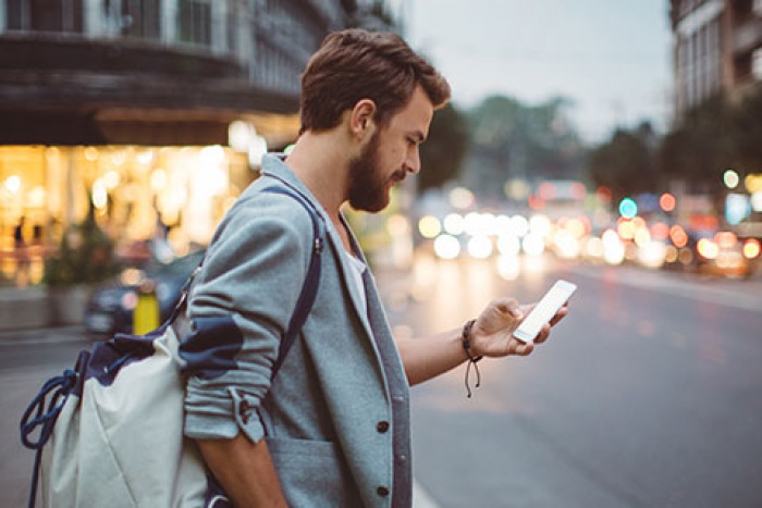 man carrying backpack on a busy street while looking at his cell phone