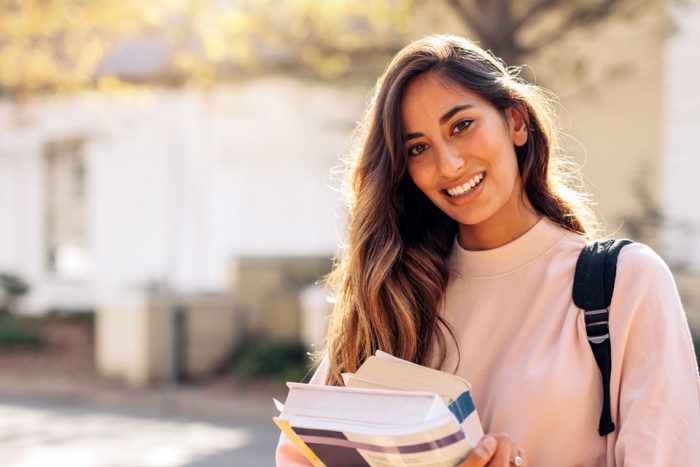 young woman holding textbooks carrying backpack